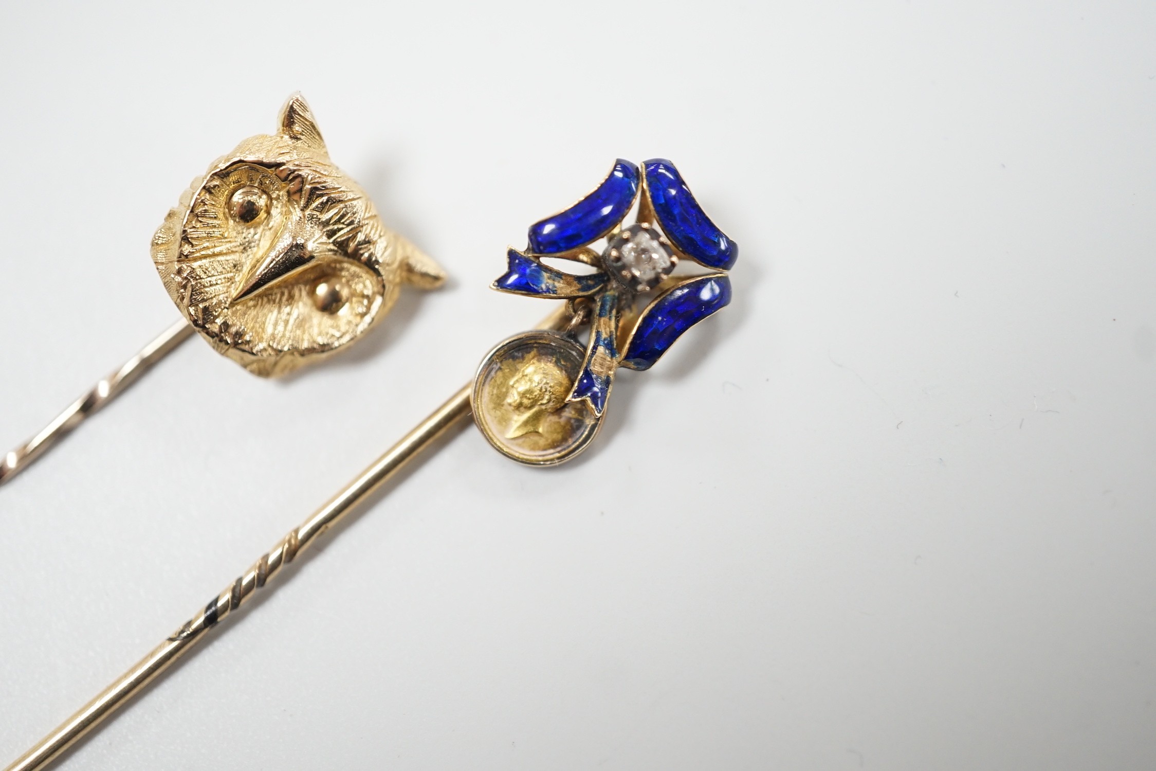 An early 20th century yellow metal enamel and diamond set ribbon bow stick pin, hung with a miniature medallion, 63mm and a later 9ct gold stick pin, gross 5.2 grams.